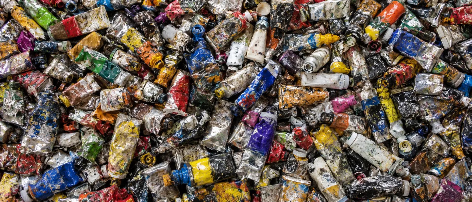 A pile of used oil paint tubes, dented and smeared with paint, seen from above